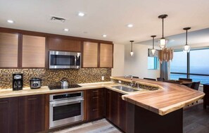 Une cuisine moderne avec des meubles en bois foncé, des appareils électroménagers en acier inoxydable et un grand îlot central doté d’un évier intégré.