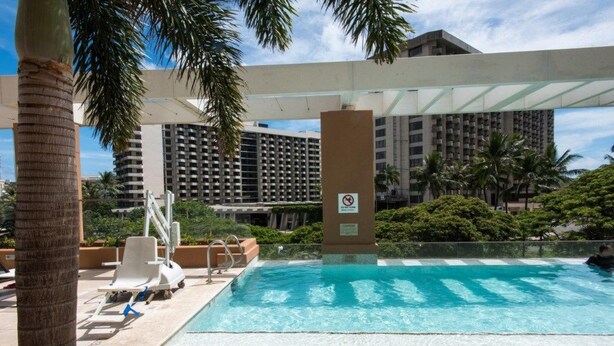 A swimming pool with lounge chairs, palm trees, and a building in the background.