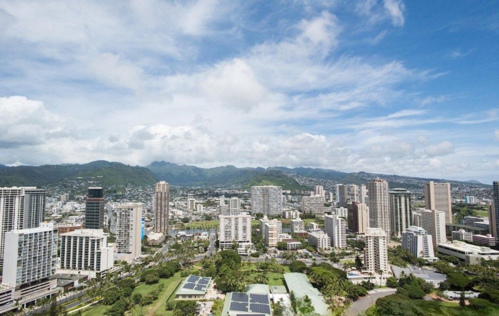 Une vue urbaine avec de hauts immeubles, des espaces verts et des montagnes en arrière-plan.