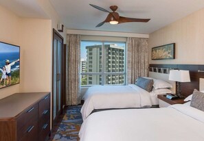 A hotel room with two beds, a ceiling fan, a large window with curtains, a TV, and a painting on the wall.