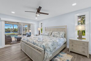 A bedroom with a bed, a ceiling fan, a nightstand, a lamp, and a view of a pool and outdoor furniture. - beautiful views and sunsets in the gorgeous ground level home! (Sanibel)