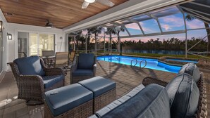 Un espace aménagé au bord de la piscine, avec des meubles en osier et une vue sur la piscine et les arbres.