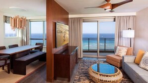 Un salón amplio con una gran mesa de comedor, asientos cómodos, televisión y vista al océano.