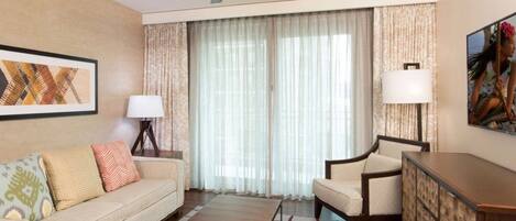 A hotel room with a sofa, armchair, wooden coffee table, and a ceiling fan.