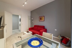 A modern living room with a glass dining table, a red sofa, and a painting on the wall.