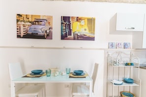 A dining area with a glass table, chairs, and a metal shelf with dishes.