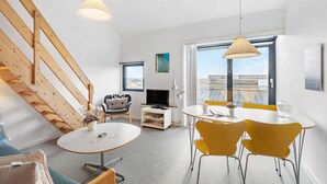 Ein modernes Wohnzimmer mit Essbereich, einer Holztreppe und großen Fenstern mit Blick auf die Stadt.