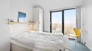 Ein Schlafzimmer mit einem Bett, einem gelben Sessel, einem Fenster mit Aussicht und einem Schrank.