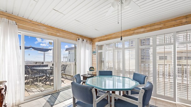 A sunlit room with a glass table and blue chairs, large windows with blinds, and a view of a patio with outdoor furniture. - ⭐️Fountain Head Beach Bungalows steps to Beach Pool⭐️ (Ocean City)