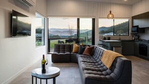 Ein modernes Wohnzimmer mit einer Eckcouch, einem runden Couchtisch und einem großen Fenster mit Blick auf die Landschaft.