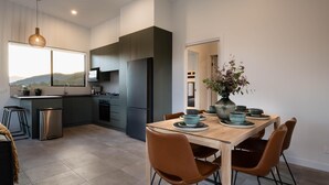 Eine moderne Küche mit dunklen Schränken, einem Edelstahlkühlschrank und einer Essecke mit Holztisch und braunen Stühlen.