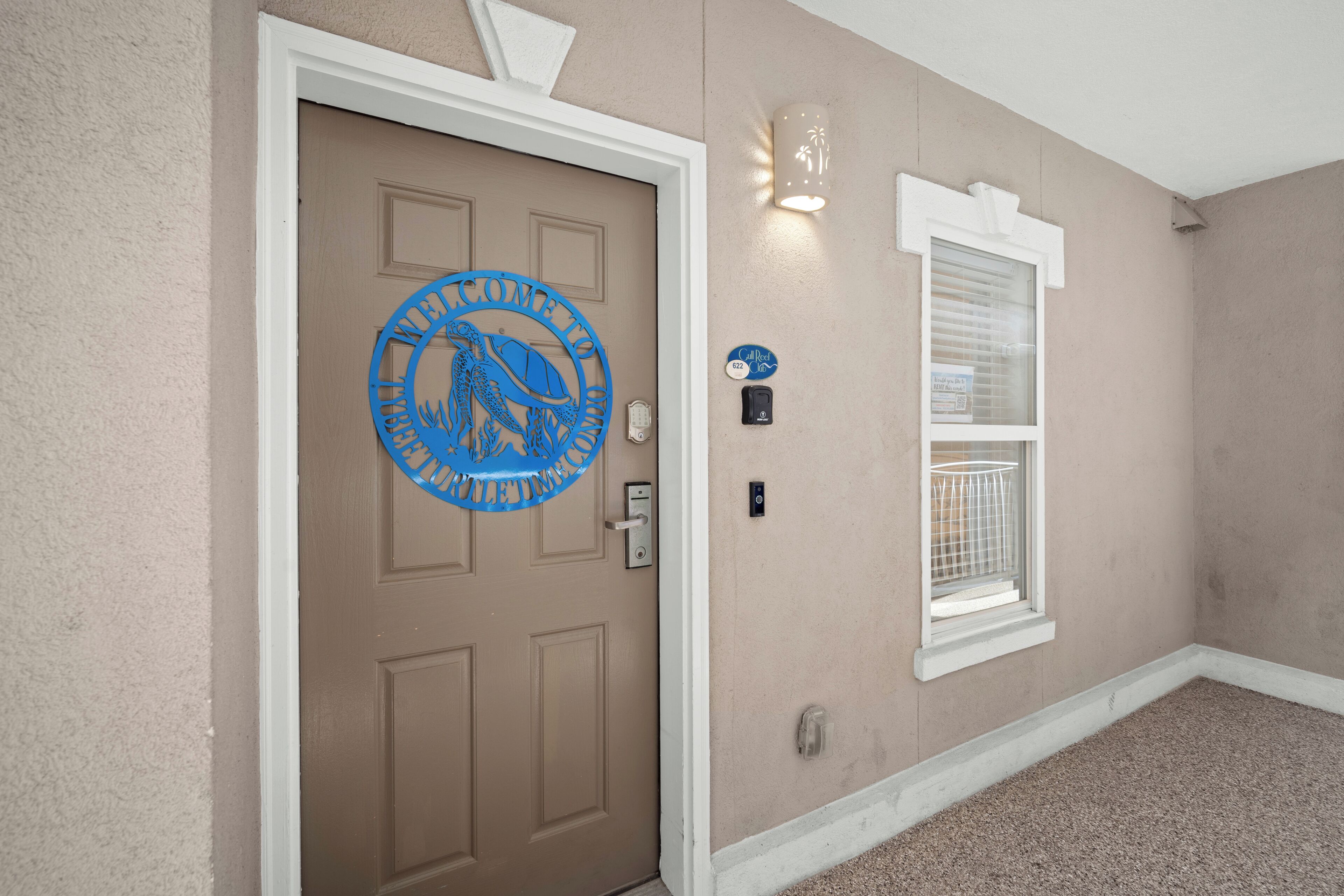 A beige door with a blue welcome sign, a window with a white frame, and a light fixture on the wall.