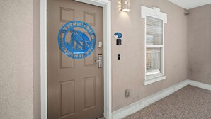 A beige door with a blue welcome sign, a window with a white frame, and a light fixture on the wall. - Tybee Beachfront Condo, 2 Pools & Restaurant, 1–3BR Flexibility, Turtle Time (Tybee Island)