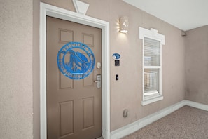 A beige door with a blue welcome sign, a window with a white frame, and a light fixture on the wall. - Tybee Beachfront Condo, 2 Pools & Restaurant, 1–3BR Flexibility, Turtle Time (Tybee Island)