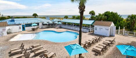 A pool area with lounge chairs and umbrellas, a lifeguard station, and a view of the ocean.