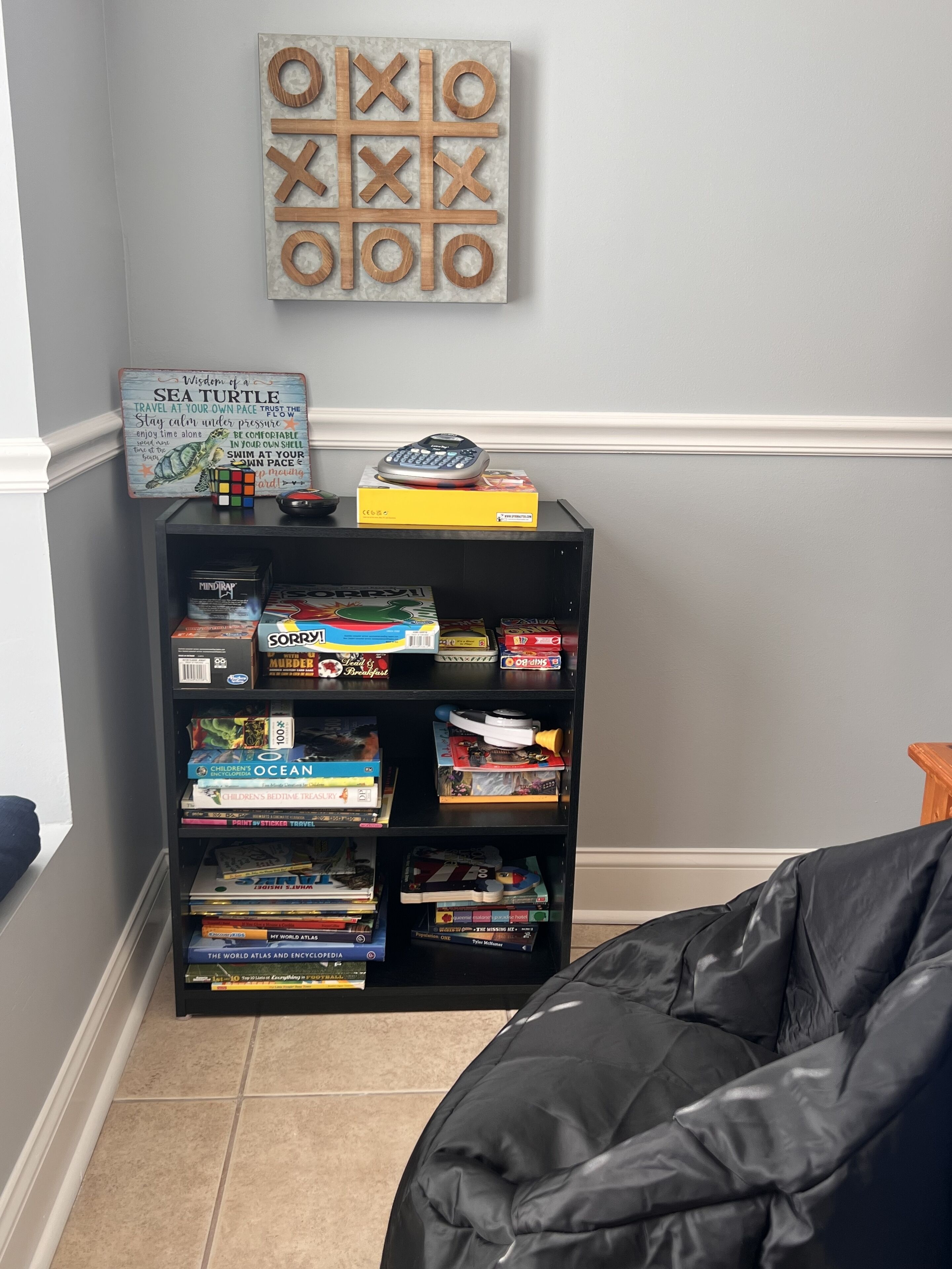 A room with a bookshelf filled with books, a Rubik's cube, and a Sea Turtle Wisdom sign.