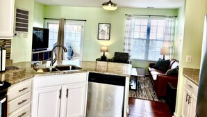 A kitchen with white cabinets, a dishwasher, and a television. There is a dining area with a couch and a lamp. - Townhome in Village of 5 Points, 3BDR 2.5BA Sleeps 6-8. Saturday-Saturday (Lewes)