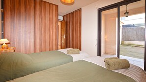 Ein Hotelzimmer mit zwei Betten, einem Holzschrank, einer Lampe und einer Schiebeglastür nach draußen.