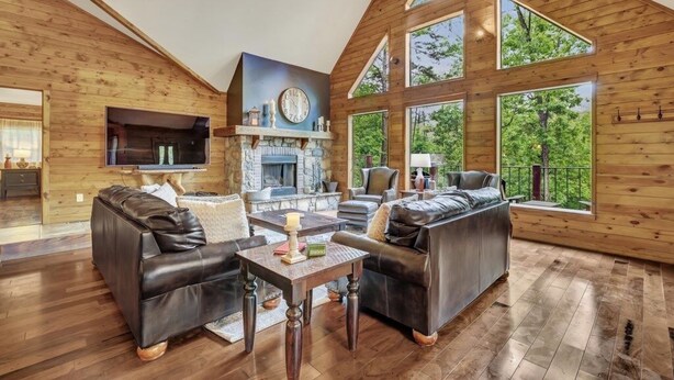 A spacious living room with a stone fireplace, leather sofas, and large windows offering a view of the outdoors.