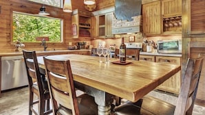 A rustic kitchen with wooden cabinets, a large wooden table, and hanging pendant lights.