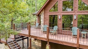 A cabin with a wooden deck, outdoor seating, and a staircase leading to an upper level.
