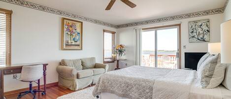 A bedroom with a bed, a desk, a chair, a sofa, a ceiling fan, and a view of the outdoors.