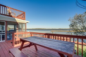 Enjoy a serene view of the water from this deck with a picnic table and railing, surrounded by lush greenery.