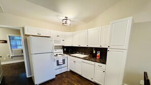 Una cocina con armarios blancos, un refrigerador blanco, una estufa y un microondas.