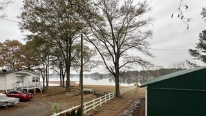 Una propiedad junto al lago con una casa blanca, un garaje cubierto y un patio cercado con árboles de Navidad.