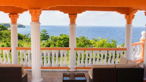 Un espacio de estar al aire libre cubierto, con columnas blancas y barandales naranja, con vistas a un paisaje marino.