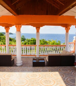 A covered outdoor seating area with white columns and orange railings, overlooking a scenic ocean view.