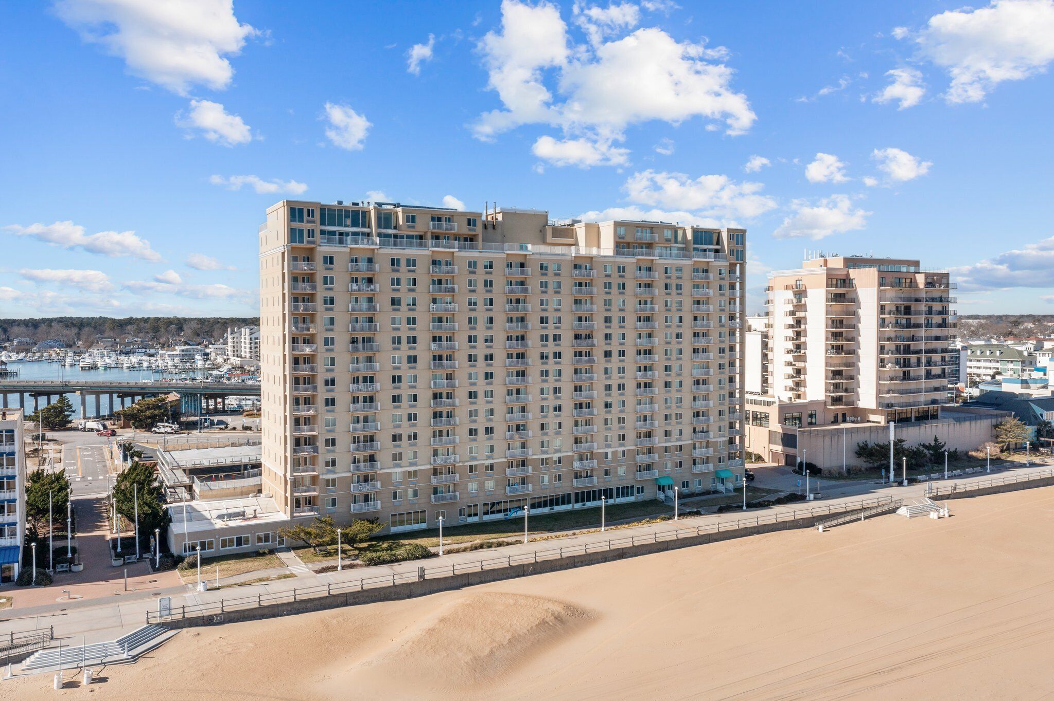 Un grand hôtel à plusieurs étages, une marina en arrière-plan et une plage de sable au premier plan.