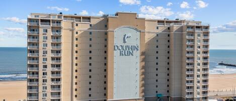 A large, multi-story hotel with a prominent 'DOLPHIN RUN' sign, located near a beach with a clear view of the ocean.