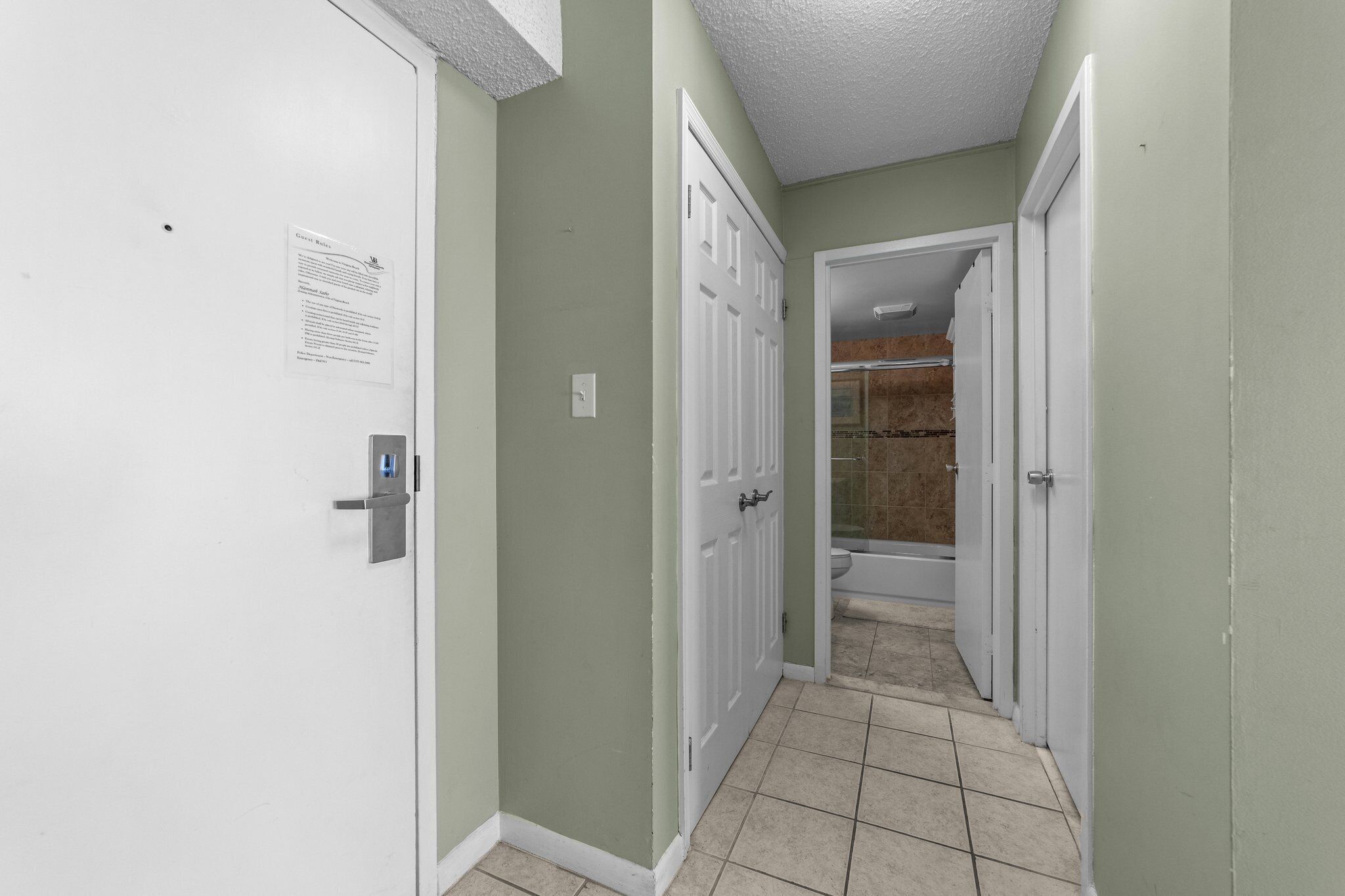 Un couloir étroit avec des portes blanches, un sol carrelé et une salle de bain visible, équipée d’une douche et de toilettes.