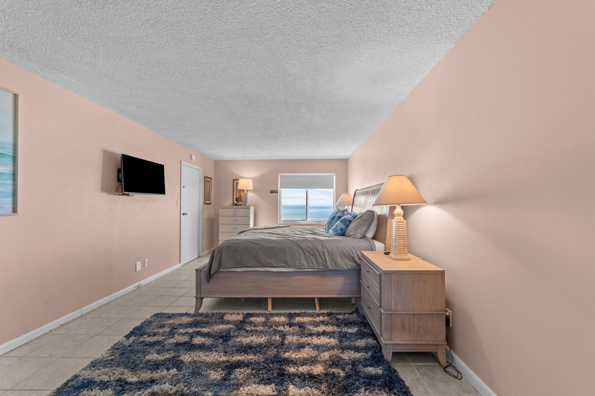 A bedroom with a bed, bedside table, lamp, and a TV mounted on the wall.