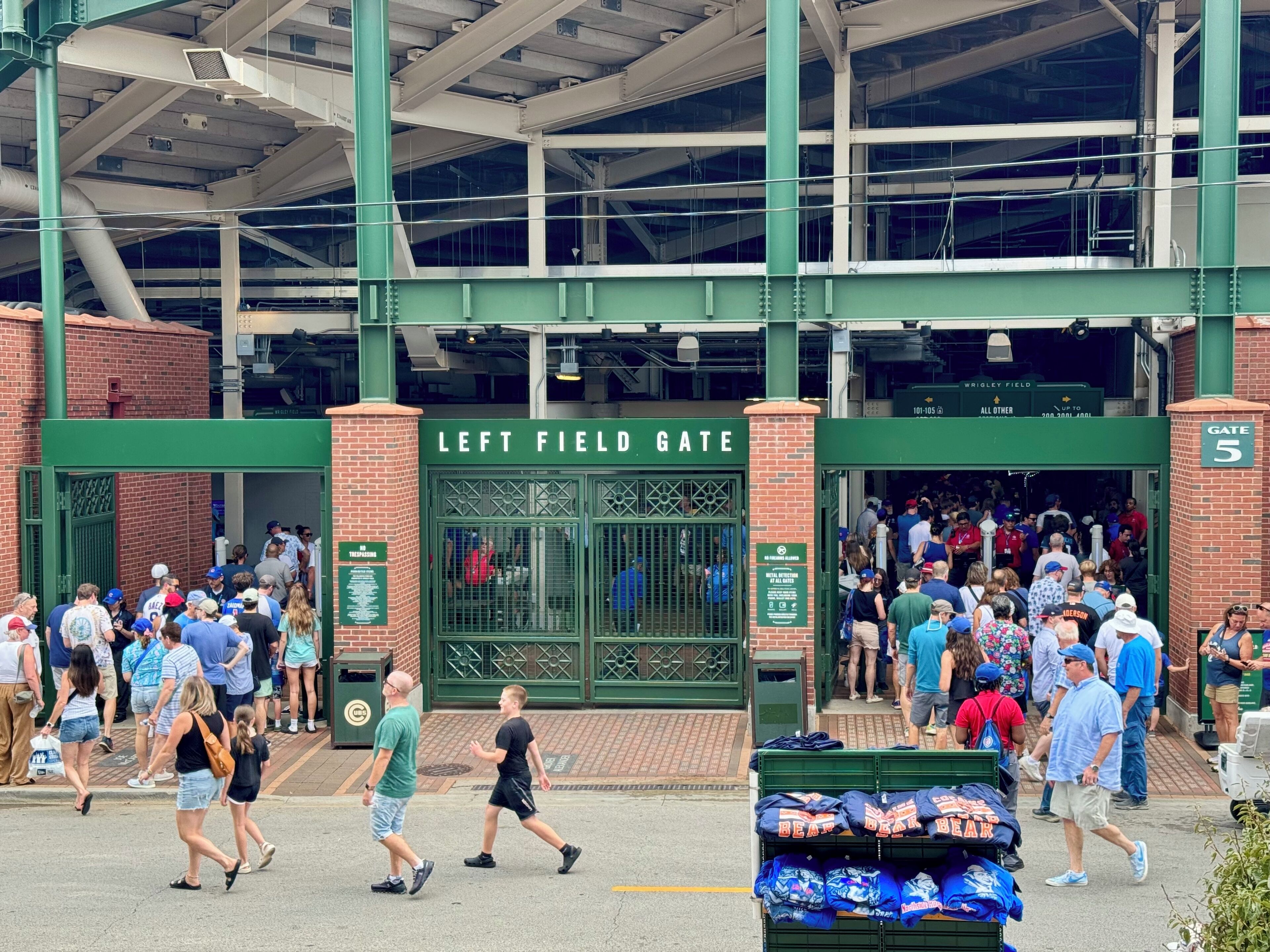 Une entrée de stade avec une pancarte indiquant « PORTAIL DU CHAMP GAUCHE » et une foule de personnes qui y pénètre.
