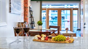 Un plan de travail en marbre sur lequel est disposée une assiette de fruits, deux verres de vin rouge et une planche à découper en bois.