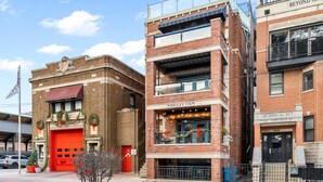 Un immeuble à plusieurs étages avec une porte rouge de caserne de pompiers, un balcon illuminé et une enseigne indiquant « Wrigley View ».