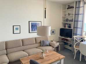 A living room with a sofa, a coffee table, a TV, and a bookshelf. - Direkt am Meer, Näher Dran Geht Nicht! - Haus Irma (Wyk auf Föhr)