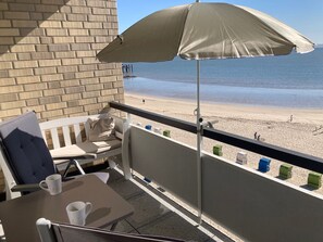 Ein Balkon mit Blick auf den Strand, ein Tisch mit zwei weißen Tassen und ein beiger Sonnenschirm.