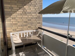 A balcony with a white bench and table, a beach view, and a brick wall. - Direkt am Meer, Näher Dran Geht Nicht! - Haus Irma (Wyk auf Föhr)