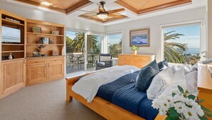 A bedroom with a bed, wooden cabinets, a TV, and a balcony with a view of the ocean.