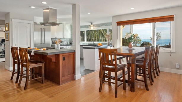 A modern kitchen with a central island, wooden chairs, and a view of the ocean.
