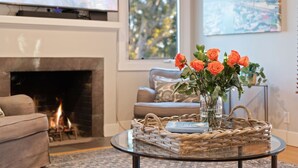 A living room with a fireplace, a sofa, a coffee table with a basket and vase, and a painting on the wall.