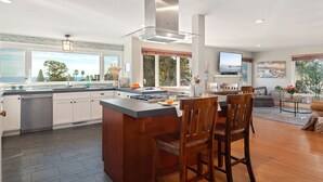 A modern kitchen with an island, large windows, and a dining area with chairs.