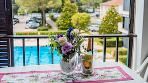 En balkon med et bord dækket til to personer, med en blomstret dug, en vase med blomster, to vinglas og en vinflaske.