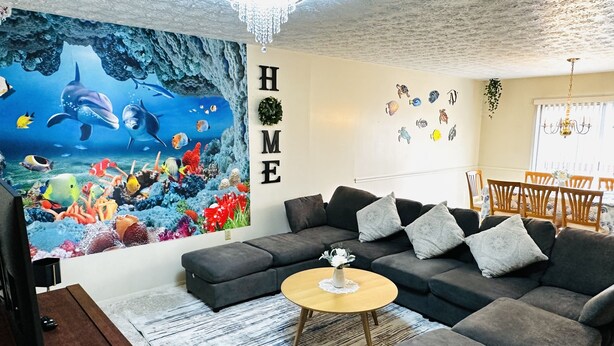 Un salon agrémenté d’une grande fresque représentant un aquarium, d’un canapé gris foncé, d’une table basse ronde et d’un lustre.
