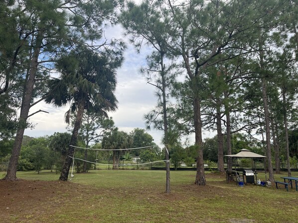 Un parque con cancha de voleibol, mesas de picnic y zona de barbacoa.