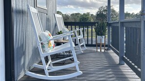 A wooden porch with two rocking chairs, a potted plant, and a doormat with a message.