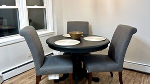 Un comedor con una mesa redonda, cuatro sillas tapizadas en gris, piso de madera y una araña.